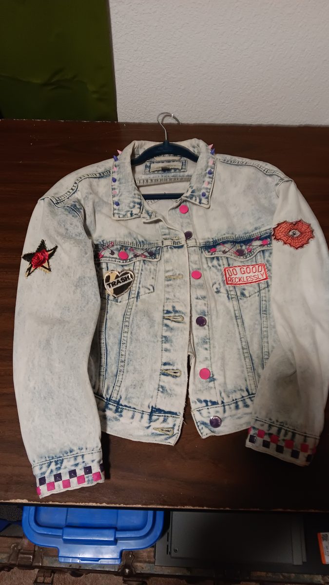Do Good Recklessly jacket — front view with pink studs, checkered cuffs, Trash pin, and Do Good Recklessly patch
